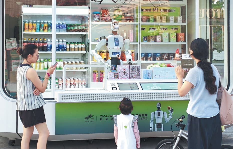Passers-by stop to watch a humanoid service robot working in a self-service retail kiosk.