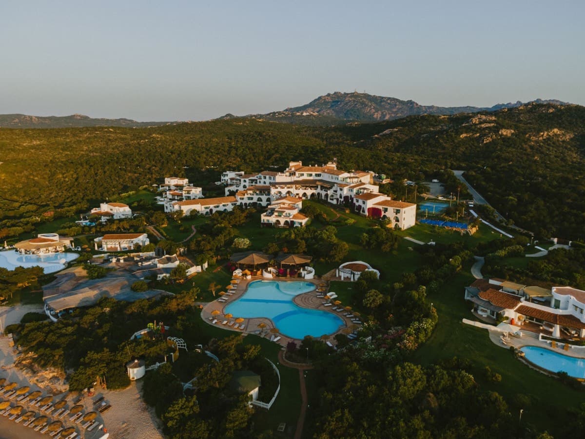 撒丁岛翡翠海岸上 Romazzino, A Belmond Hotel 的日落航拍全景,泳池与度假村掩映在绿意之中。
