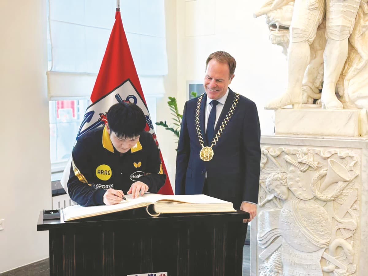Inside Dusseldorf's City Hall, Fan Zhendong bends over to sign the Golden Book as Mayor Stephan Keller looks on with a smile.