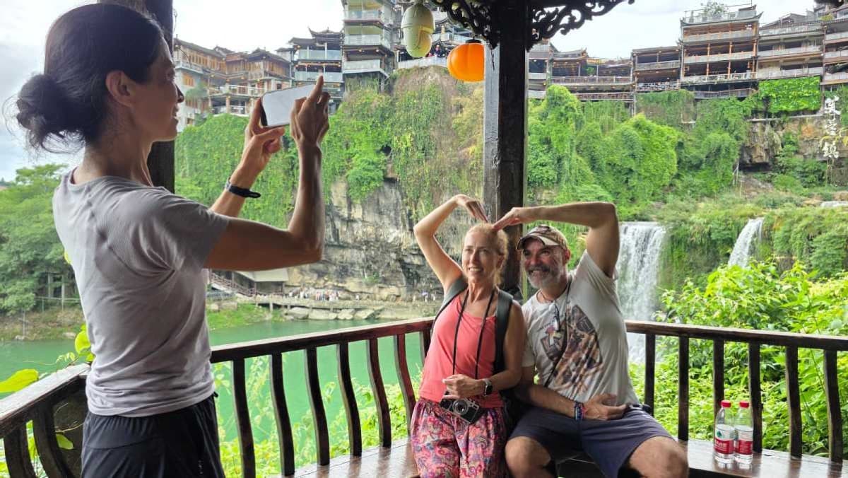 Foreign tourists take photos in a stilt house by the waterfall in Furong town, Hunan.