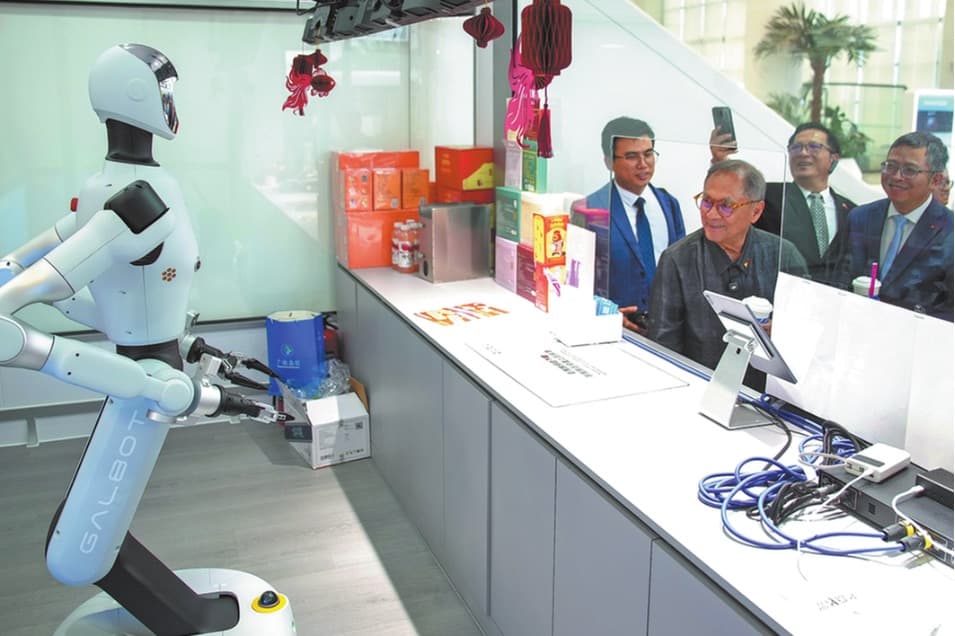 A Galbot humanoid robot works at a self-service retail counter as a delegation looks on.