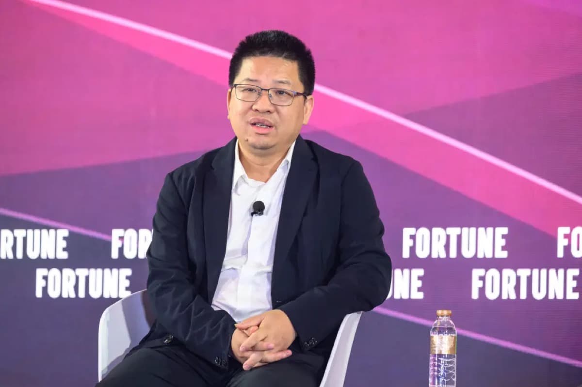 A man sits on a stage for an interview against a pink and purple backdrop repeatedly printed with the FORTUNE logo.