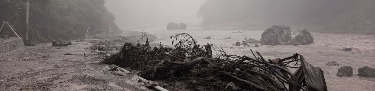 Under heavy fog, the riverbed near Gyirong port is choked with rocks, broken branches and debris swept down by the mudslide, as muddy floodwater continues to churn.