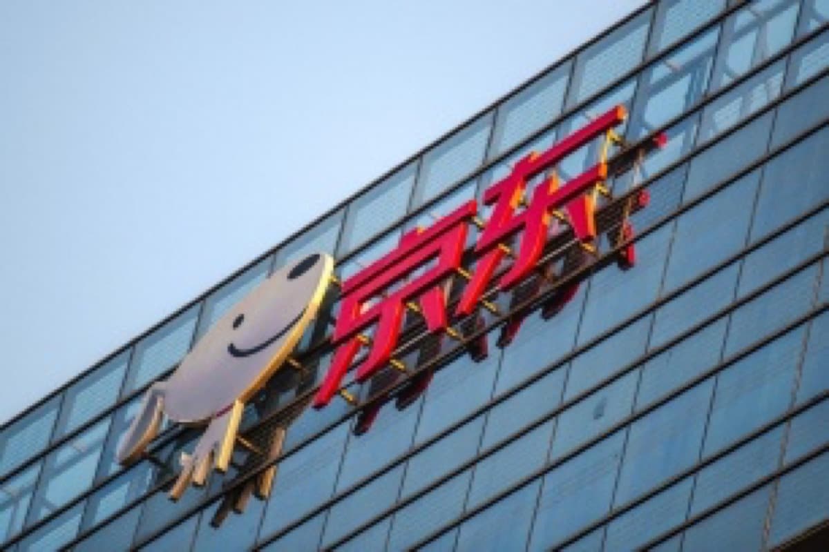 The JD.com logo, a red wordmark beside a cartoon dog mascot, mounted on the glass facade of the company's headquarters building.