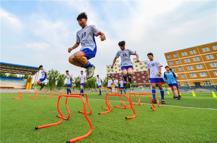 Students run hurdle drills during after-school football practice on a sports field