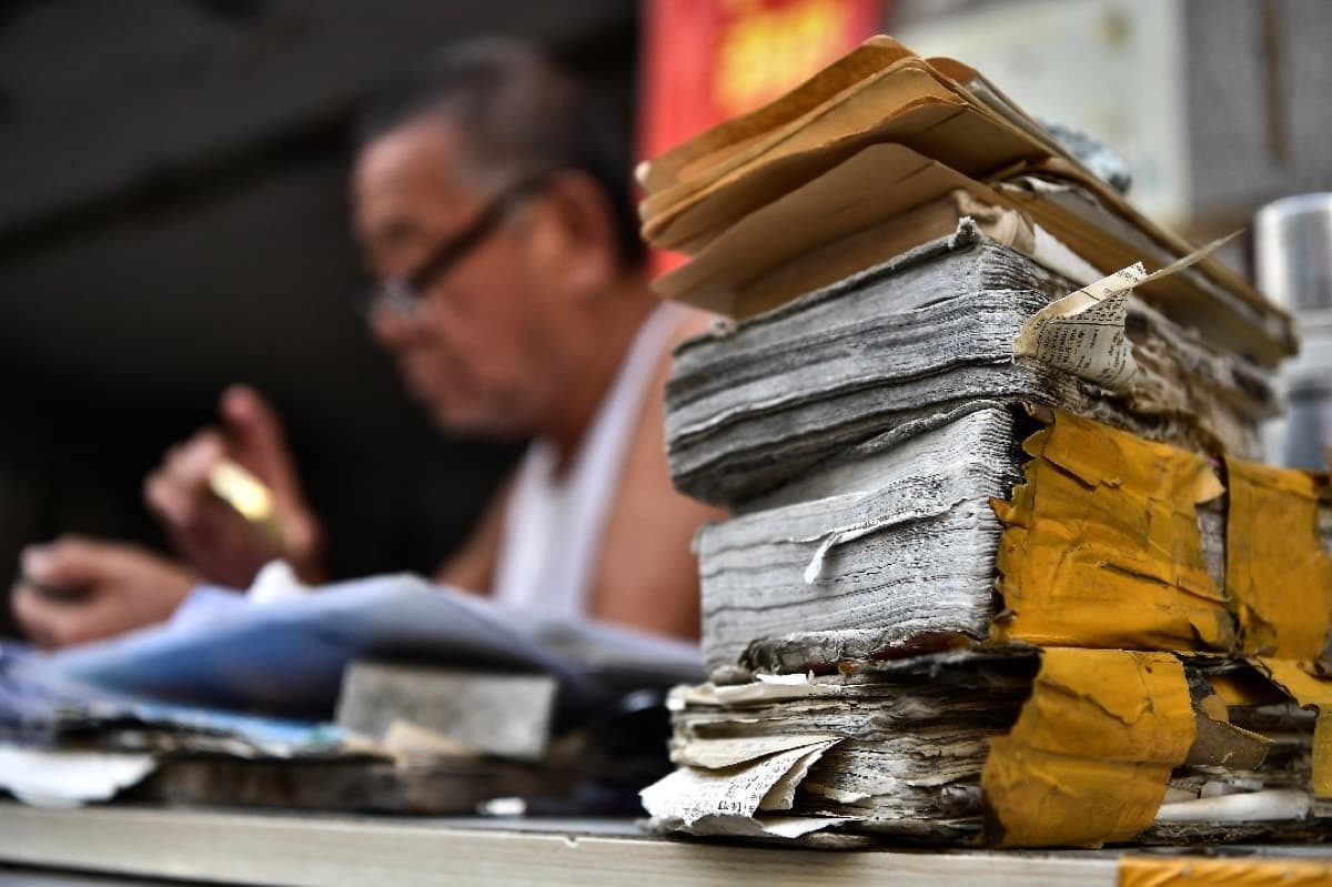 A qiaopi letter-writer works at his table in Shishi, Fujian, beside stacks of worn old ledgers.