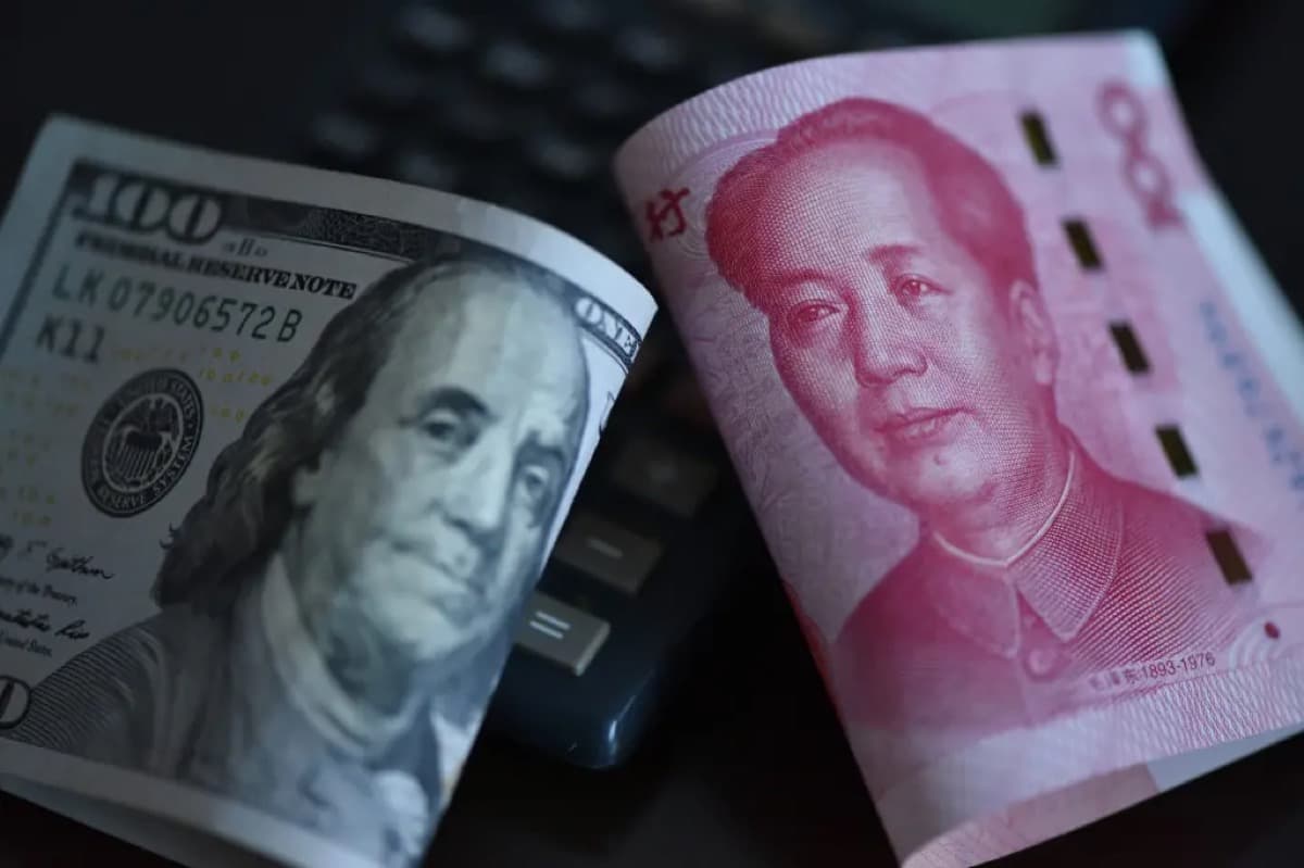 一张百元美钞与一张人民币纸币并排放置在计算器上,钞票上的头像形成鲜明对比。