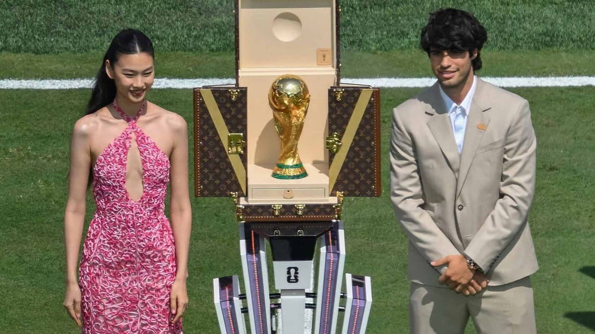 The World Cup trophy on display on the pitch, flanked by two guests