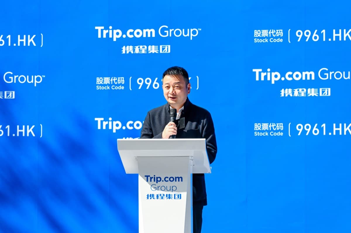 A Trip.com Group executive speaks at an event in front of the company's branding and stock code.