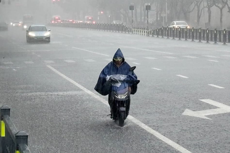 A rider in a poncho pushes through heavy rain on a city road.