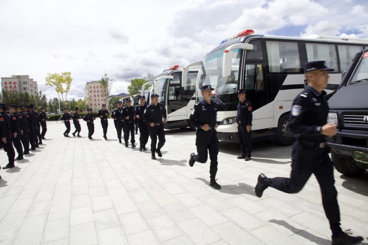A group of police officers line up in front of a row of patrol buses and vehicles before jogging off on duty, under a cloud filled sky.